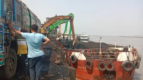 Shore equipment and trucks beside a barge carrying bulk material