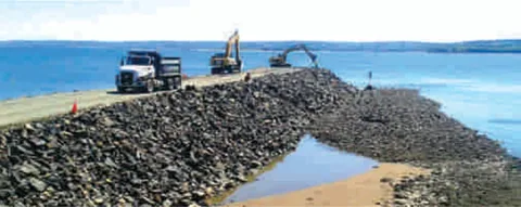 Trucks and excavators building a rock breakwater beside the sea