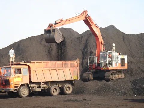An orange excavator loading coal into a tipper truck