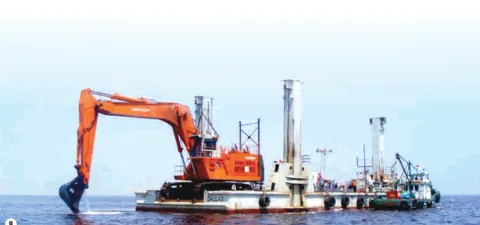 An excavator on a floating platform alongside a workboat