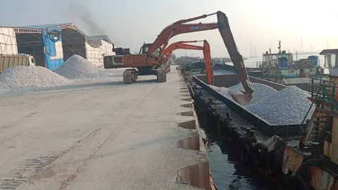 Excavators loading white bulk material into barges beside warehouse sheds
